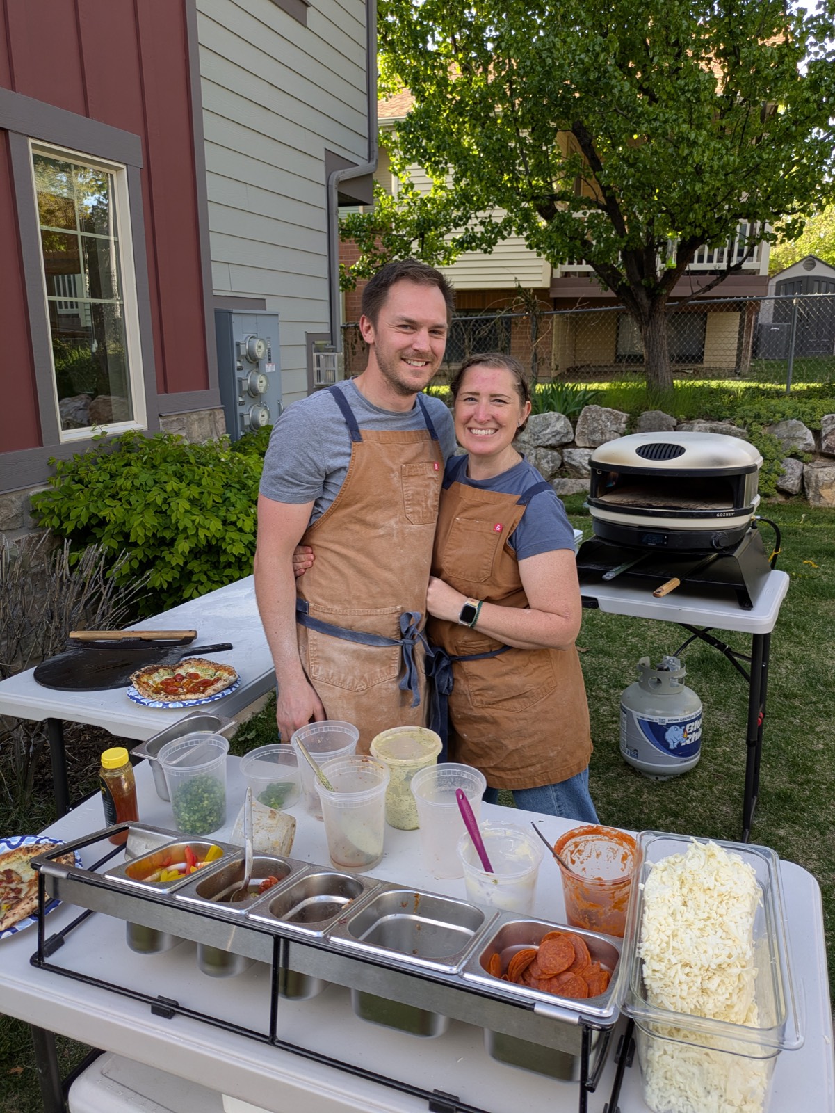 Backyard Brick Oven owners at their mobile pizza topping station with a fired-up brick oven